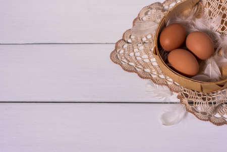 three brown chicken eggs lie in a wicker container on a knitted lace napkin on a white wooden background horizontal photo with place for textの写真素材