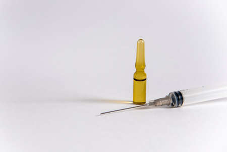 Dark yellow glass ampoule with liquid stands behind a lying medical syringe on a white backgroundの写真素材