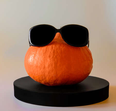 an orange round pumpkin with black glasses on a low black podiumの写真素材