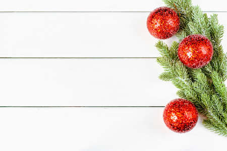New Year's composition made of artificial green spruce branches with shiny red Christmas balls on the right on a white wooden horizontal background with a place for textの写真素材