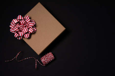 cardboard gift box with a red and white bow with red and white braid on a black ibl background on...