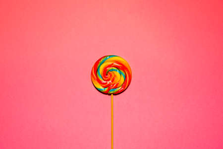 bright multicolored round lollipop in the center on a pink backgroundの写真素材