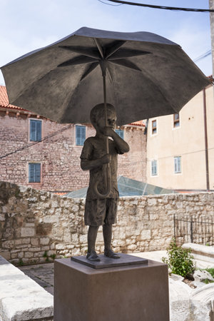 Sibenik, Croatia - May 26, 2022- the iron statue of a small boy holding an umbrella, a tourist attraction in the old streets of the townÂ のeditorial素材