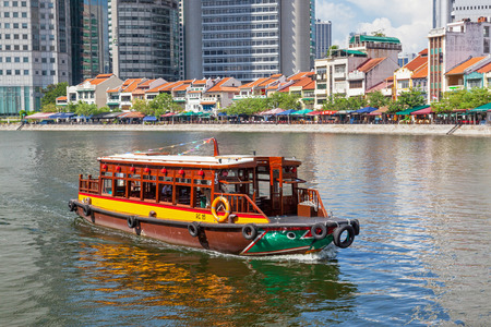 A traditional bumboat (water taxi) at Boat Quay, a historical quay in Singapore, situated upstream from the mouth of the Singapore River on its southern bank. The city's financial district is situated in the background.のeditorial素材