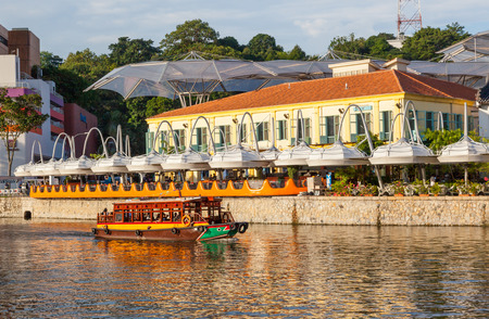 A traditional bumboat laden with tourists motors past Clarke Quay on the Singapore River.のeditorial素材