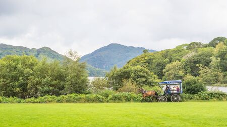 KILLARNEY, IRELAND - AUGUST 13, 2019: Tourists in a traditional jaunting car explore Killarney National Park in County Kerry, Ireland. Muckross Lake lies in the background.のeditorial素材