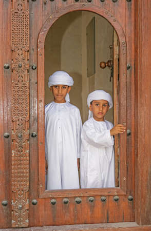 SHARJAH, UAE - APRIL 14, 2005: Two brothers in national dress, at the door of a restored house in the Sharjah Heritage Area, on their way to Sharjah's Heritage Days Festival.のeditorial素材