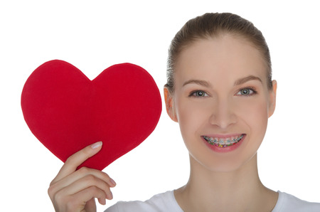 Happy girl with braces on teeth and red heart isolated on whiteの写真素材