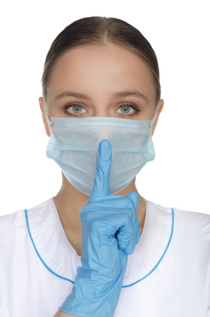 Vertical portrait of doctor in mask and gloves with your finger from the lipsの写真素材