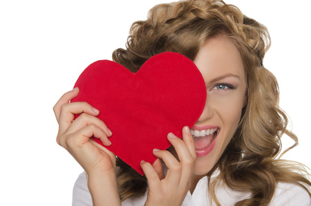 Smiling beautiful young woman holding heart in front of eyeの写真素材