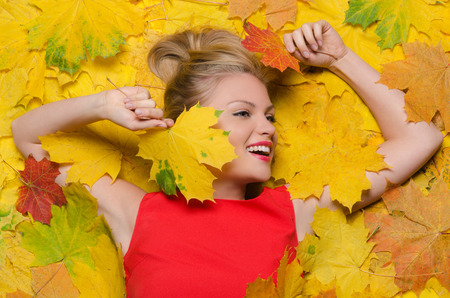 Beautiful smiling woman in yellow autumn maple leavesの写真素材