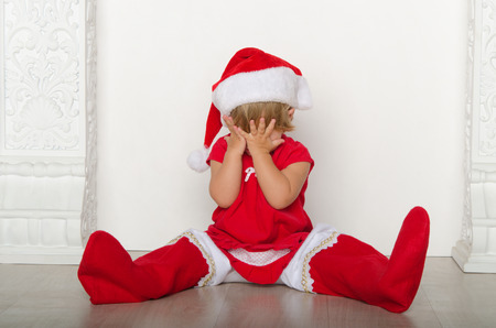 little girl in costume of Santa hides his faceの写真素材