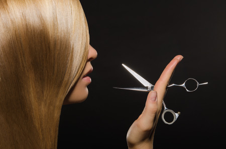 Beautiful woman with straight hair and scissors on black background