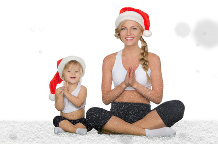 woman with child doing yoga in Christmas hats under the falling snowの写真素材