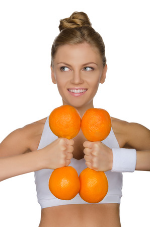 young girl holding a dumbbell of ripe oranges and looks to the side isolated on whiteの写真素材