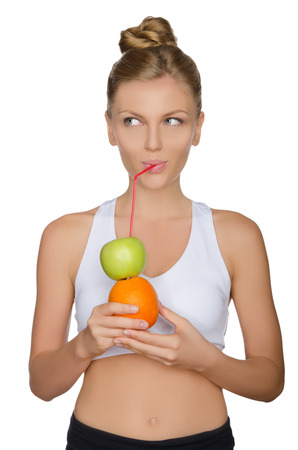young  woman drinking juice from apple and orange isolated on whiteの写真素材