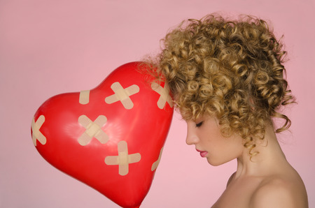 hurt woman with ball in shape of heart on pink backgroundの写真素材