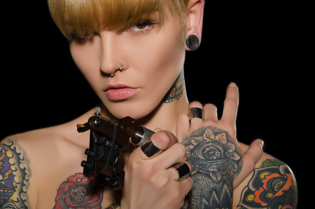 tattooed charming woman with tattoo machine, dark backgroundの写真素材