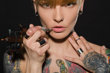 charming blonde with tattoo machine and for them, dark backgroundの写真素材
