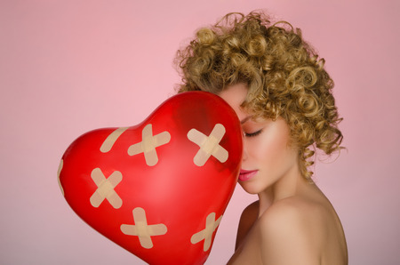 Unhappy young woman with ball in shape of heart on pink backgroundの写真素材