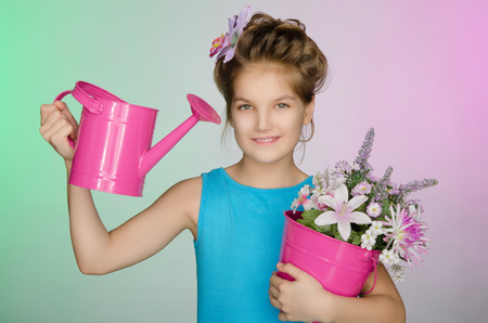 Happy girl with watering can and beautiful flowers on colored backgroundの写真素材