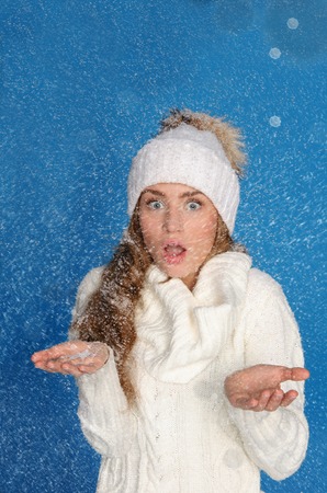 Surprised woman in winter clothes with snow on blue backgroundの写真素材