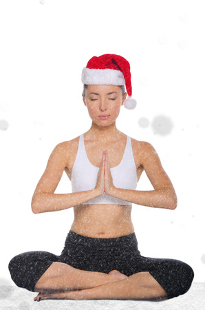 concentrated asian woman in christmas hat with snow practicing yoga isolated on whiteの写真素材