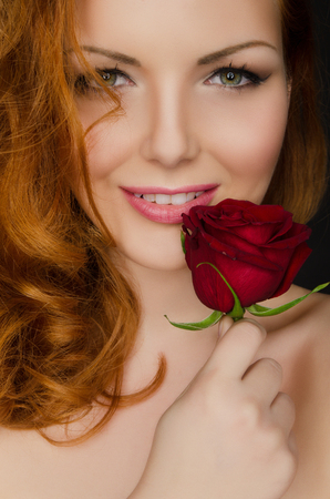 Young woman with red hair holds red rose in her handsの写真素材