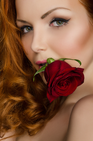 woman with long red hair holds beautiful rose in her mouthの写真素材