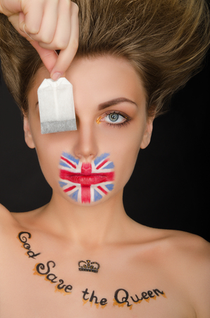 Woman with english flag on face and tea bag, black backgroundの写真素材