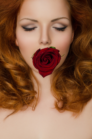 Red rose in the teeth of woman with long hairの写真素材