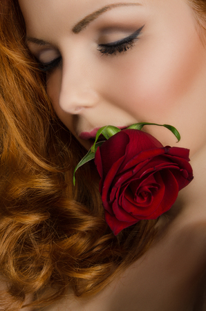 young woman with curly red hair holds beautiful rose in her mouthの写真素材