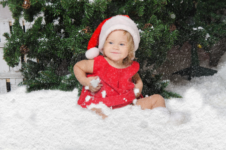 smiling girl in santa costume sits on white snowの写真素材