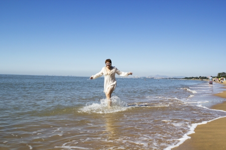 middle-aged woman in a white dress running along the edge of the seaの写真素材