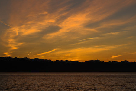 Picture of sunset over the sea with mountains and cloudsの写真素材