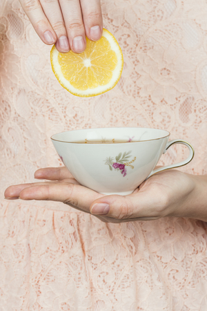 Woman holding a cup of tea in hand and adding a slice of lemonの写真素材