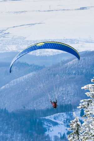 POIANA BRASOV, ROMANIA - JANUARY 24, 2016: Paragliding instructor taking off the ski slope and flying in tandem over the mountain resort Poiana Brasov in Romaniaのeditorial素材