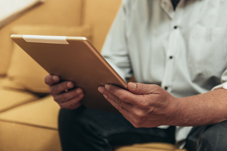 Hands of a senior man using a digital tablet in a cozy homeの写真素材