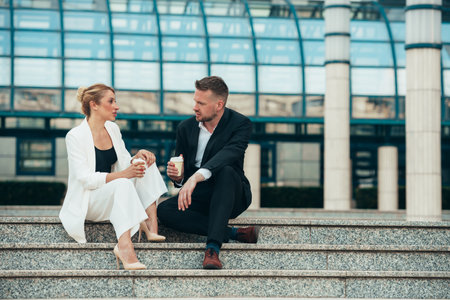 Two businesspeople drinking coffee on their break from work while sitting on a stairsの写真素材