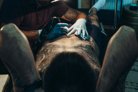 Shot of a tattoo artist with his client in a studio while holding a machineの写真素材