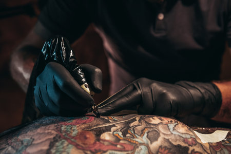 Tattoo artist hands wearing black protecting gloves and holding a machine while creating a tattoo on a man skinの写真素材