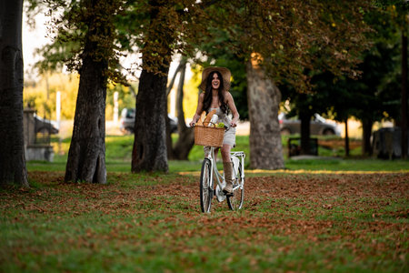 A happy young woman riding a vintage bicycle with basket full of groceries in the park with a bicycleの写真素材