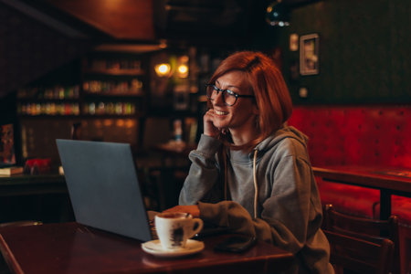 Young redhead woman using a laptop while drinking coffee and working in a cafeの写真素材