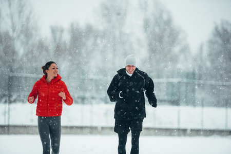 Young couple going for a run together during a snow on a cold winter day