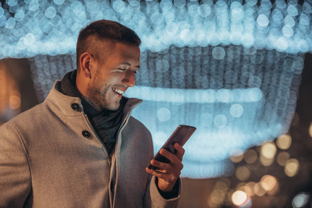 Cropped shot of a handsome young man using his smartphone while walking in the city streets in the winterの写真素材