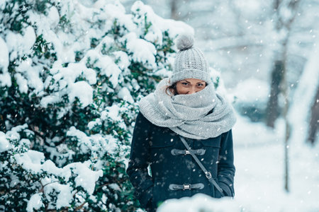 Beautiful young woman wearing scarf and a a hat on a cold winter day during snowの写真素材