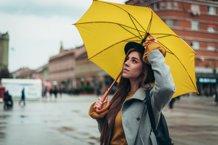 Young beautiful woman holding a yellow umbrella during a walk on a rainy dayの写真素材