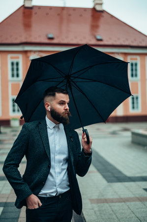 Young handsome businessman holding a black umbrella while walking in the city on a rainy dayの写真素材