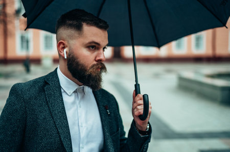 Young handsome businessman holding a black umbrella and listening music on   while walking on a rainy dayの写真素材