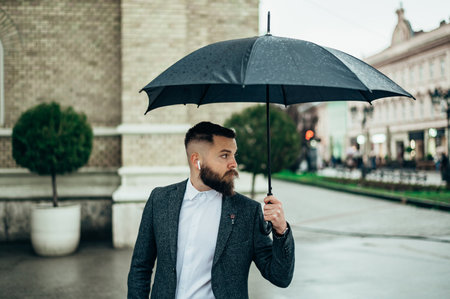 Young businessman using and holding a black umbrella while out in the city on a rainy dayの素材 [FY310196189545]